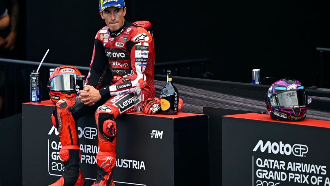 רוכב MotoGP בחליפת מרוץ אדומה יושב על מדרגת הפודיום בגראז' אחרי מרוץ