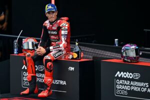 רוכב MotoGP בחליפת מרוץ אדומה יושב על מדרגת הפודיום בגראז' אחרי מרוץ